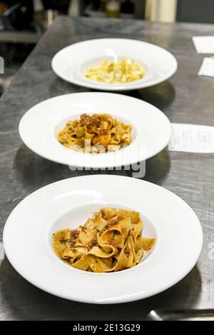 Ciotole su un banco ristorante con tagliatelli italiani conditi con pasta con una salsa di ragù pronta per servire ai clienti Foto Stock