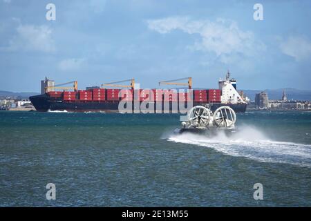 L'hovercraft Solent Flyer che attraversa il Solent a Portsmouth da Ryde sull'isola di Wight con la nave portacontainer Independent Vision davanti ad essa. Foto Stock