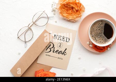 Scheda con testo HO BISOGNO DI UNA PAUSA, busta e tazza di caffè su sfondo bianco Foto Stock