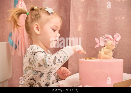 Una bambina in pigiama al suo compleanno si siede su una sedia bianca ad un tavolo per bambini, su cui c'è una nascita Foto Stock