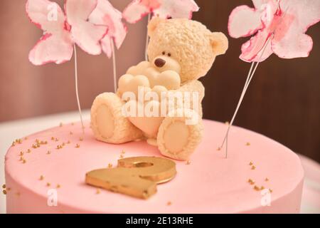 Torta di compleanno rosa rotonda per un bambino di 2 anni. Orsetto di cioccolato bianco con cuori sulla torta Foto Stock