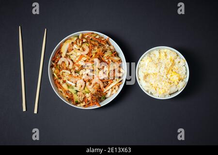 Piatto vibrante di insalata di gamberi, ciotola di riso con uova e bastoncini di pollo su sfondo nero. Togliere il cibo. Foto Stock