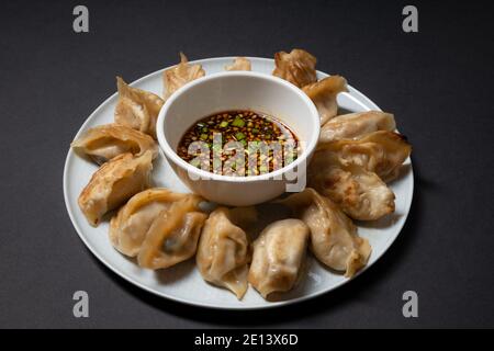 Gnocchi in stile gyoza fritti in un piatto con salsa di soia piccante su fondo nero. Asporto cibo asiatico. Foto Stock