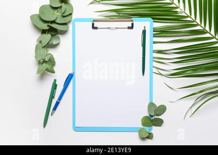 Appunti con foglio di carta vuoto e foglie verdi su bianco sfondo Foto Stock