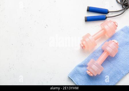 Eleganti manubri, asciugamano e corda da salto su sfondo chiaro Foto Stock