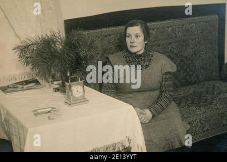 Lettonia - CIRCA anni '30: Ritratto a corpo pieno di donna seduta su divano vicino al tavolo. Foto d'epoca Art Deco d'epoca Foto Stock