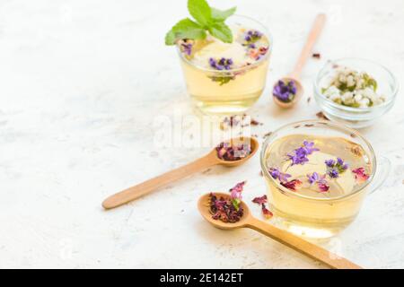 Tazze con tè floreale ed erbe in cucchiai alla luce sfondo Foto Stock