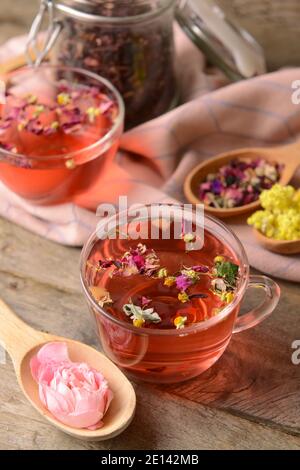 Tazza di tè floreale e cucchiai con fiori secchi sfondo di legno Foto Stock