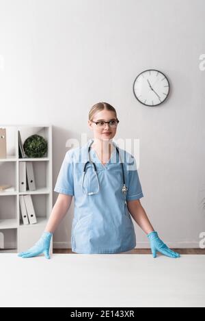 buon giovane veterinario in occhiali e guanti in lattice in piedi vicino luogo di lavoro Foto Stock