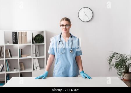 giovane veterinario in occhiali e guanti in lattice in piedi vicino al luogo di lavoro Foto Stock