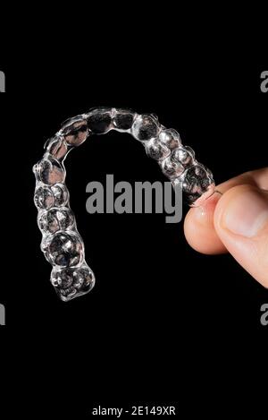 Il ragazzo tiene in mano gli allineatori trasparenti parentesi graffe in plastica fermi per raddrizzare i denti su fondo nero Foto Stock