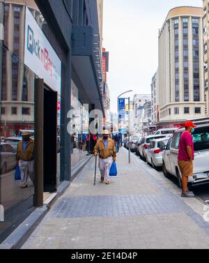 Città del Capo, Sudafrica - 23/11/2020 giorno nuvoloso a Città del Capo. Persone che si spostano per la città. Uomo anziano che indossa una maschera facciale che porta generi alimentari. Foto Stock