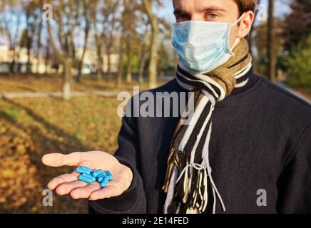 Un ragazzo in una maschera medica tiene le mani con pillole alla macchina fotografica. Foto di concetto sulla pandemia Covid 19 Foto Stock