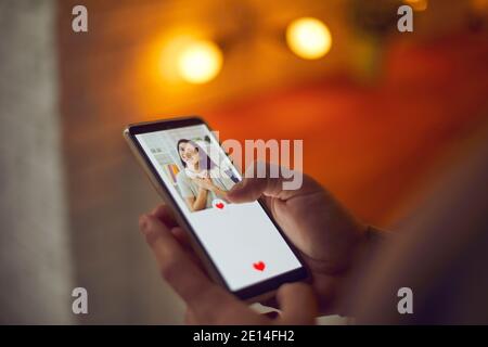 Uomo che tiene il cellulare, guardando l'immagine del profilo della giovane donna su app di incontri e premendo come Foto Stock