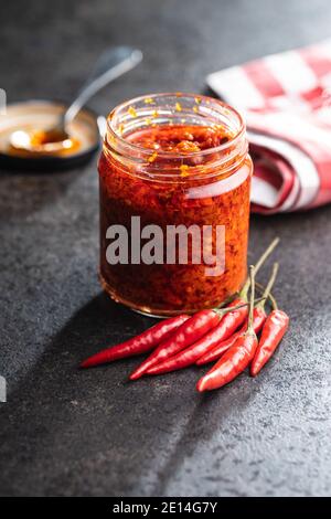 Pasta di peperoncino rosso caldo e peperoncino in vaso su tavola nera. Foto Stock