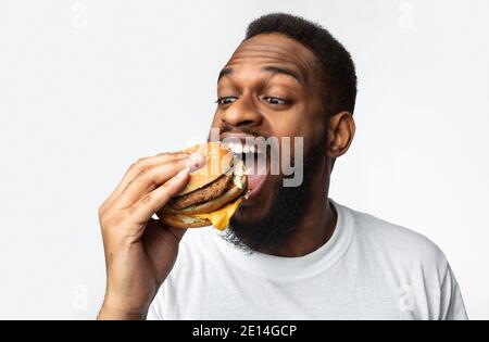 Ritratto di Hungry Black Man mangiare Burger su sfondo bianco Foto Stock