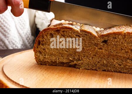 Le mani femminili tengono un coltello e tagliano il pane. Foto Stock