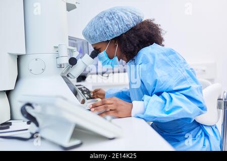 La ricercatrice femminile lavora al microscopio in laboratorio alla ricerca di vaccini Durante la pandemia di Covid-19 Foto Stock