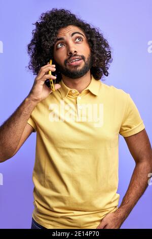 curly maschio fa un appuntamento con qualcuno che parla al telefono isolato su sfondo viola, sta guardando in su Foto Stock