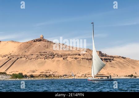 Tranquille barche a vela Felucca sul Nilo presso l'antica città egizia di Assuan precedentemente conosciuta come la città nubiana, guardando verso il sito di sepoltura e le Tombe dei Nobili e il Mausoleo collinare dell'Aga Khan. La zona è importante in quanto era un posto di sosta per l'esercito britannico che passa attraverso l'Egitto al Sudan da dove Lord Kitchener ristabilì la pace nella regione. Per questo fu dotato della terra conosciuta come Isola di Kitchener che Lord Kitchener trasformò in uno dei primi giardini botanici del mondo Foto Stock