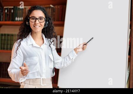 Donna sorridente in occhiali che punta alla lavagna a fogli mobili vuota Foto Stock