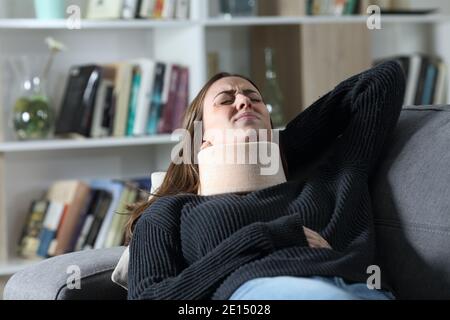 Donna disabile con sostegno al collo che lamenta dolore cervicale mentendo su un divano Foto Stock