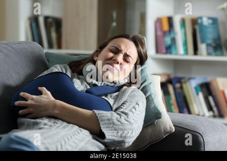 Donna che soffre di dolore con braccio rotto in un'imbragatura mentita su un divano a casa Foto Stock