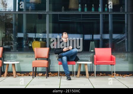il giovane si siede con uno smartphone in un caffè all'aperto Foto Stock