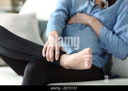 Primo piano di una donna incinta che soffre di mal di caviglia seduto su un divano Foto Stock