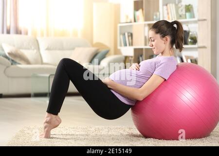 Vista laterale ritratto di una donna in gravidanza felice che fa esercizio a casa con una palla a casa Foto Stock