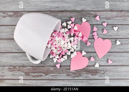 I cuori di zucchero rosa e bianco fuoriescono dal tè bianco tazza su sfondo di legno Foto Stock
