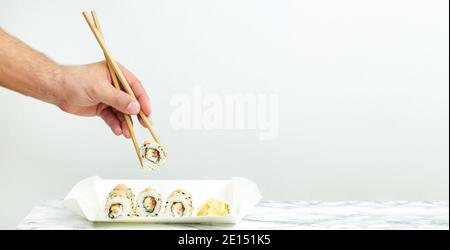 Uomo che mangia un set da portare via di sushi giapponese. Concetto di cibo per la consegna Foto Stock