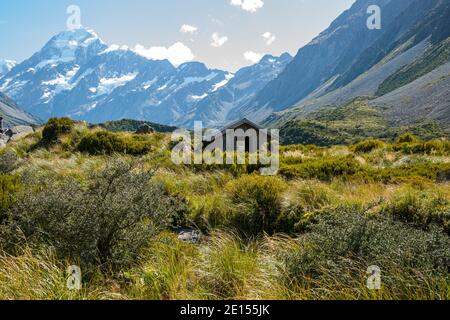 Il sole all'alba colpisce il Monte Cook innevato oltre la vegetazione alpina e la vecchia capanna storica dei tramatori sulla pista di Hookers Valley per il Lago Mueller. Foto Stock