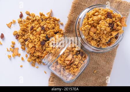 granola in un vaso di vetro e fondo bianco. la granola viene versata dal vaso Foto Stock