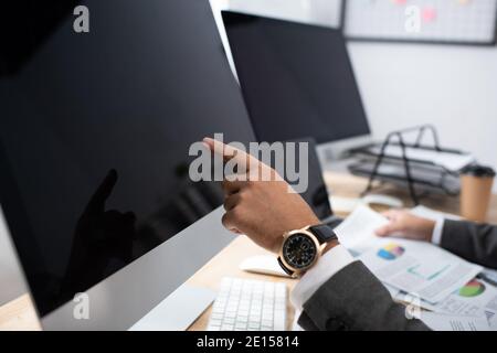 vista ritagliata del commerciante in orologio da polso puntando al monitor con schermata vuota Foto Stock