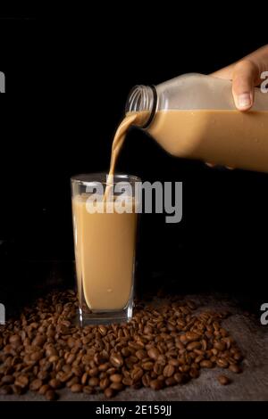 una bottiglia di latte di caffè su sfondo scuro. Il caffè tardivo viene versato nel bicchiere Foto Stock