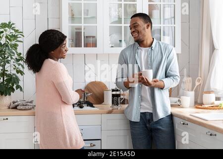 Felice coppia afroamericana che parla in una cucina accogliente, godendo di passare il tempo insieme Foto Stock