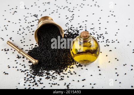 Semi di cumino nero in recipiente e olio essenziale in bottiglia di vetro. Nigella sativa isolato su sfondo bianco. Foto Stock