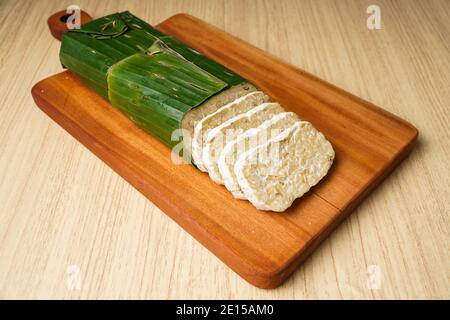 tempeh avvolto in foglie di banana e fette di tempeh su a. tagliere di legno Foto Stock