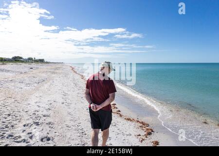 L'uomo anziano con le mani dietro le spalle cammina lungo la spiaggia di Gasparilla In Florida Foto Stock