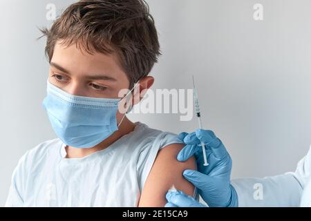 Covid 19, concetto di vaccinazione contro l'influenza o il morbillo. Ragazzo caucasico in maschera di faccia, e mano con siringa. Medico, medico o infermiere vaccina la scuola Foto Stock