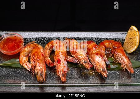 Gamberi di re fritti su una foglia di bambù, su un piatto trasparente, con limone e salsa Foto Stock