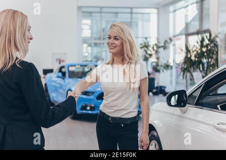 Felice bella giovane donna sorridente allegro, scuotendo le mani con il commerciante dell'automobile dopo aver acquistato la nuova automobile con successo. Venditore che si congratula con lei Foto Stock