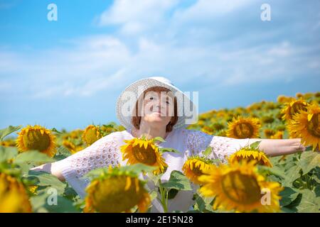 donna europea pensionata si trova in un campo con girasoli fioriti, braccia distese ai lati, stile di vita degli anziani in campagna, s Foto Stock