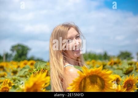 donna dai capelli dorati che sorride in un campo con fiori di girasole, felice estate in campagna, vacanza nel villaggio Foto Stock