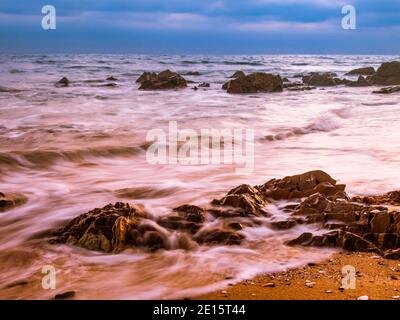 Spiaggia costa con Motion acque sfocate e rocce Foto Stock