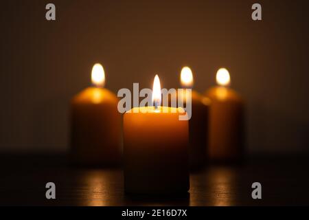 Gruppo di candele accese che bruciano nelle tenebre in oro toni con messa a fuoco selettiva su candela e sfocatura dello sfondo Foto Stock