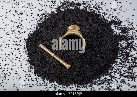 Semi di Nigella sativa noti anche come cumino nero, kalo jeera, kalonji e caraway nero in paletta di ferro e mortaio su sfondo bianco di legno con copy sp Foto Stock