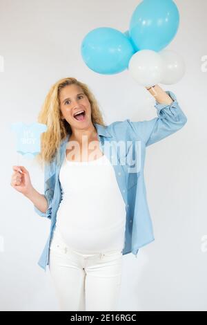 donna allegra e incinta in abiti casual che tengono palloncini isolati su bianco Foto Stock