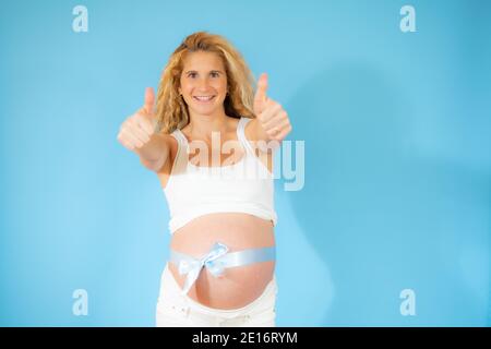 Bella donna che si aspetta un bambino, toccando la pancia incinta sorridendo positivo con i pollici verso l'alto. Espressione riuscita. Foto Stock